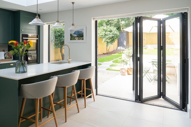 Lichte keuken met kookeiland, barkrukken en openslaande deuren naar de tuin.