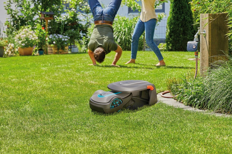 Robotmaaier op een groen gazon met spelende mensen op de achtergrond.