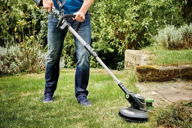 Een persoon gebruikt een grastrimmer in de tuin.