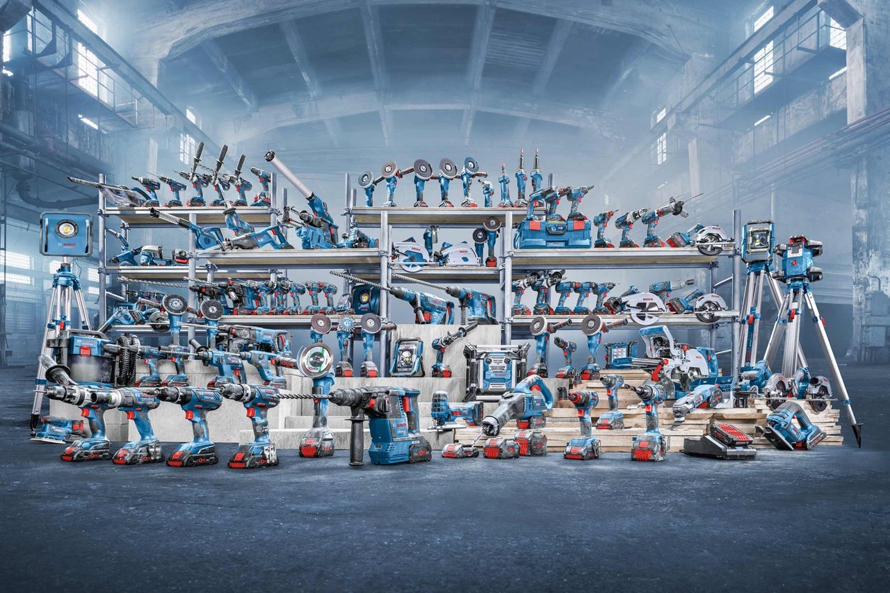 Diversiteit aan Bosch elektrisch gereedschap op planken en de vloer in een werkplaats.