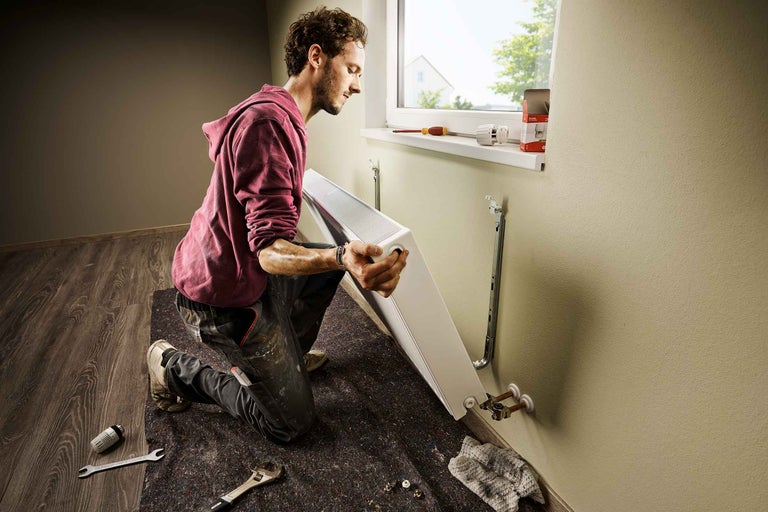 Man installeert radiator aan een muur in een kamer.