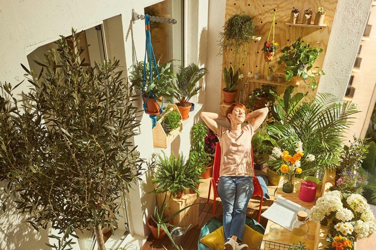 Vrouw ontspant op een zonnig balkon met planten, planken en houten elementen.