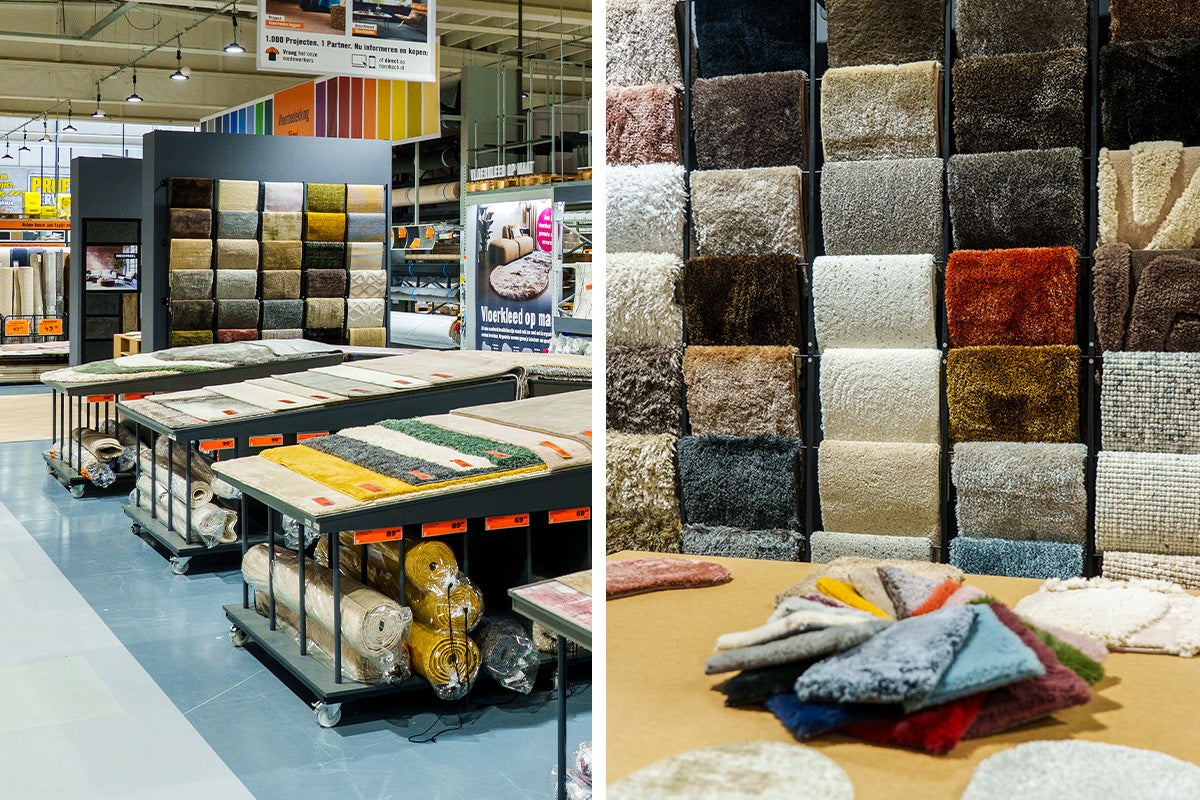 Lichte, georganiseerde tapijtafdeling met presentatietafels voor vloerkleden en wandrekken met talrijke tapijtstalen in diverse texturen.