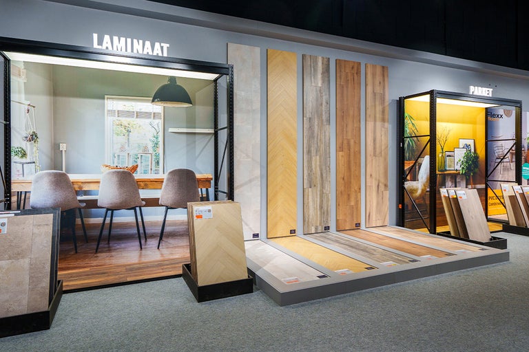 Showroom voor vloeren met monsters van laminaat en parket en een voorbeeldinterieur met een eettafel en stoelen.