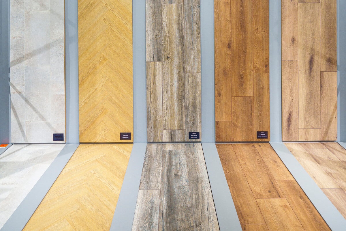 Verschillende monsters van laminaat- en vinylvloeren met houtlook, steenlook en visgraatpatroon gepresenteerd op de wand en vloer.