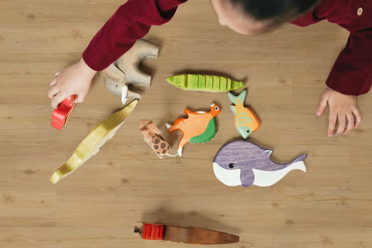 Een kind speelt met houten speelgoeddieren op een lichte vloer met houtoptiek.