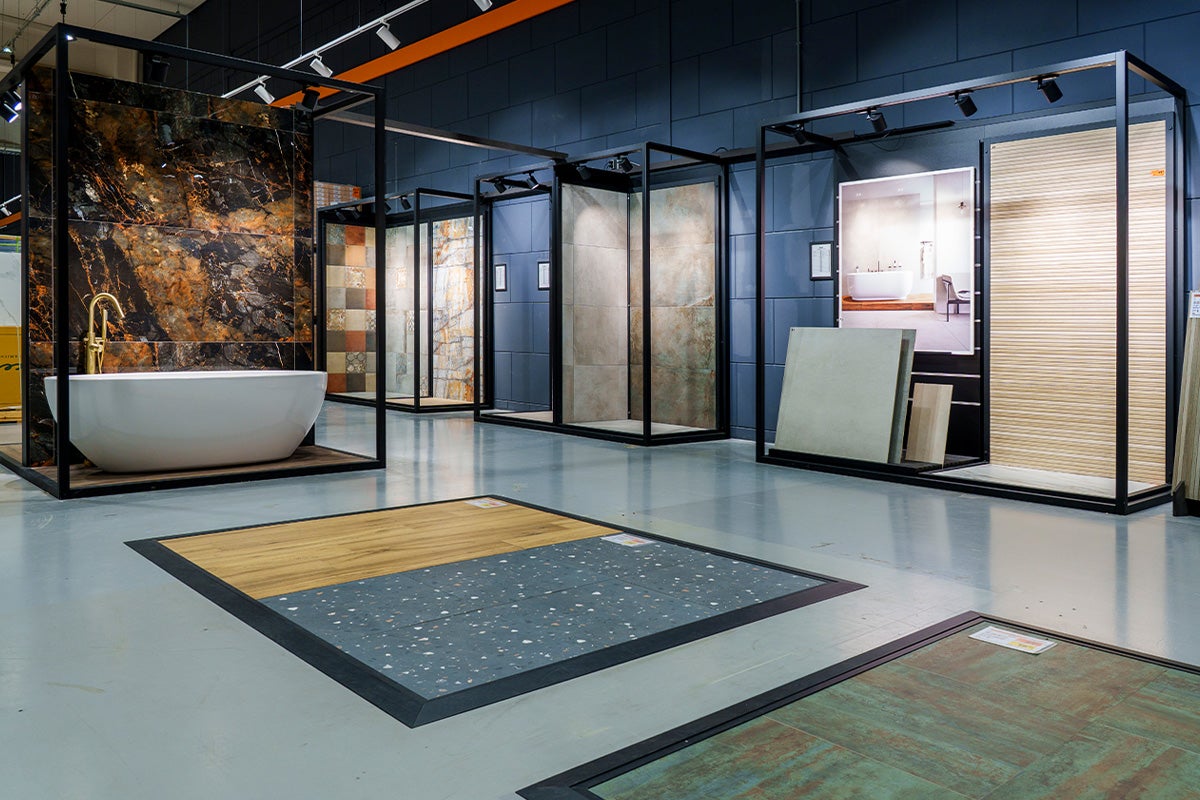 Moderne showroom voor badkamertegels met verschillende patronen op vloer en wanden en een vrijstaand wit bad.