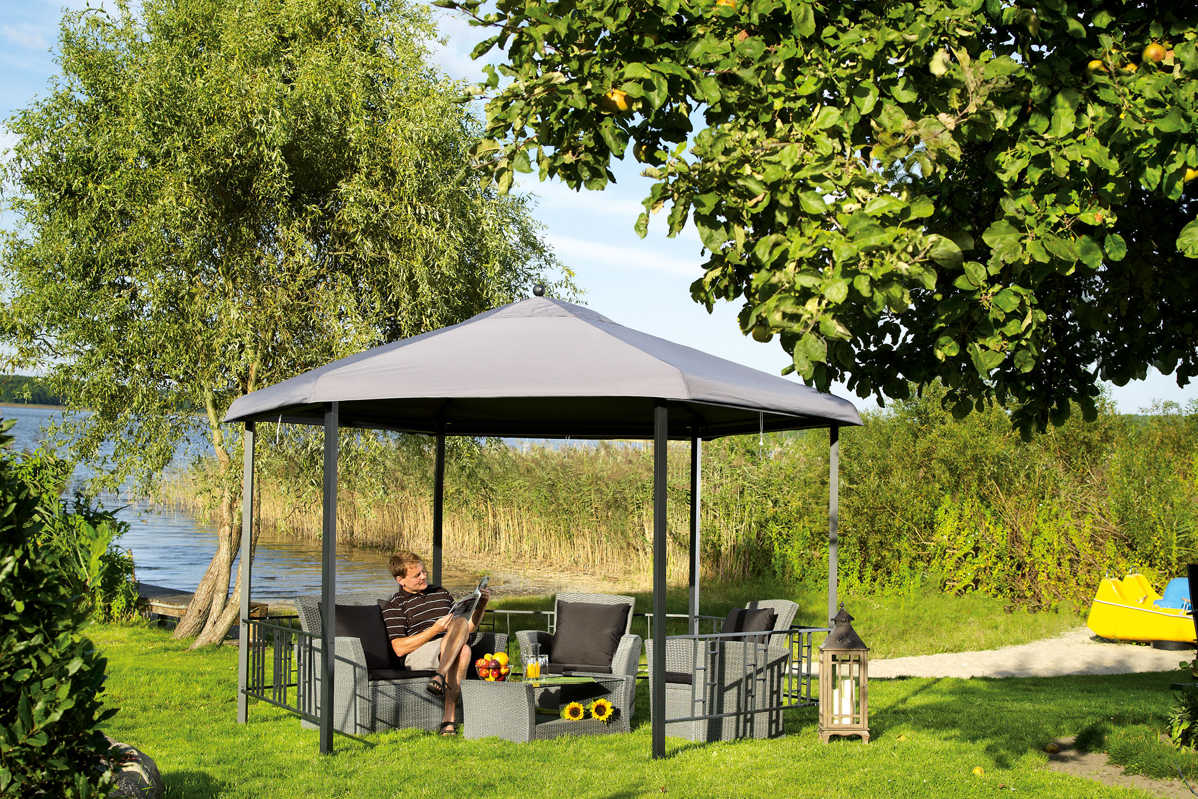 Tuinlandschap met gazebo en zittende man op een rotan zitgroep