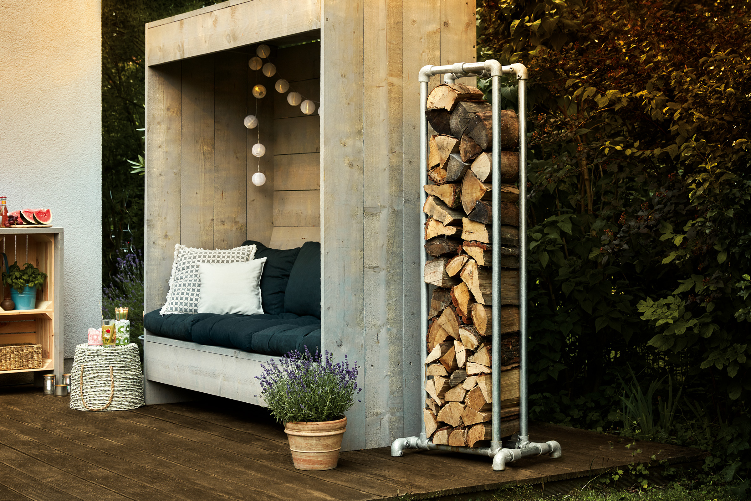 Metalen houtopslag met houtblokken naast een houten hut met zitgelegenheid op een terras