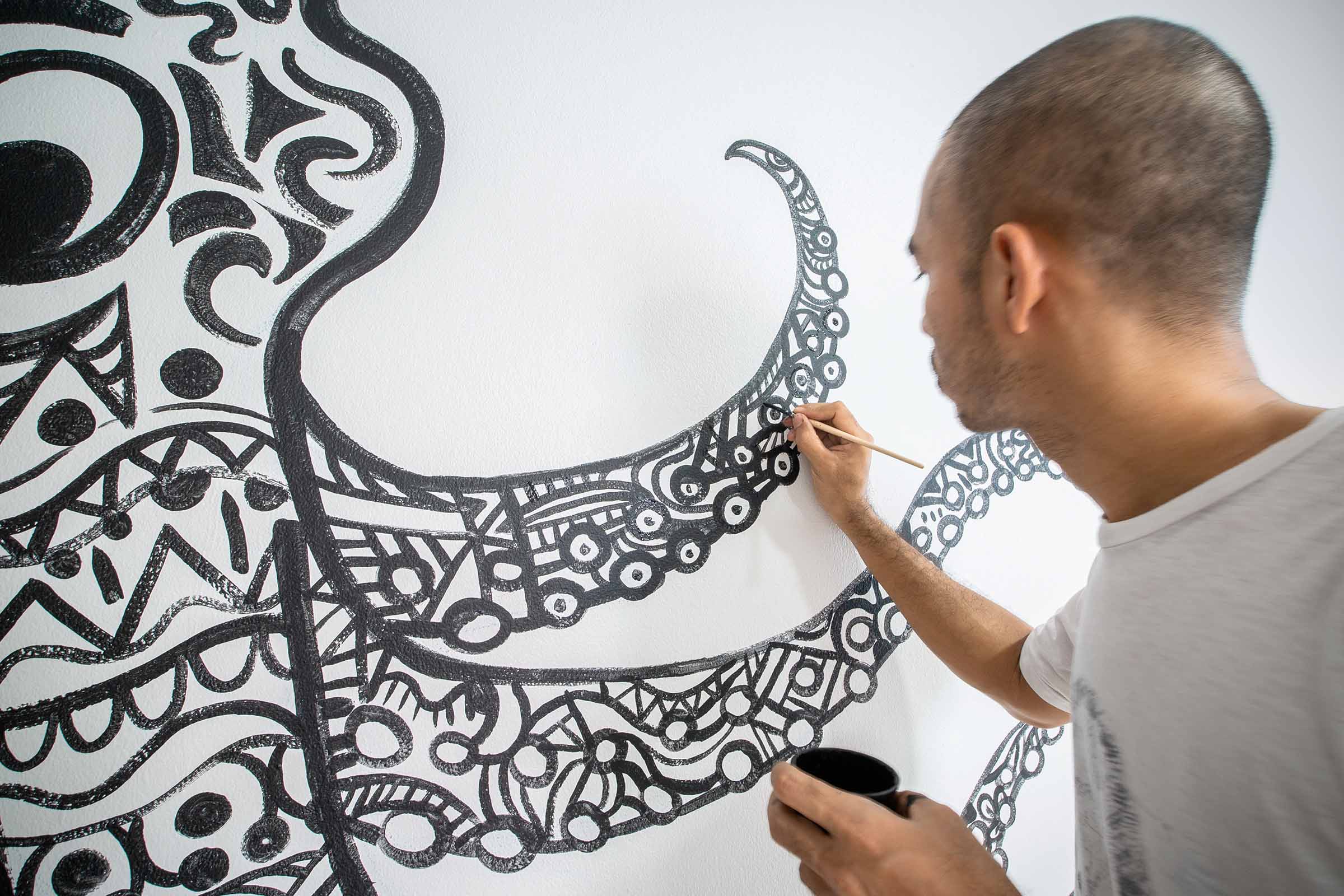 Een kunstenaar schildert met een penseel een abstract patroon op een muur.