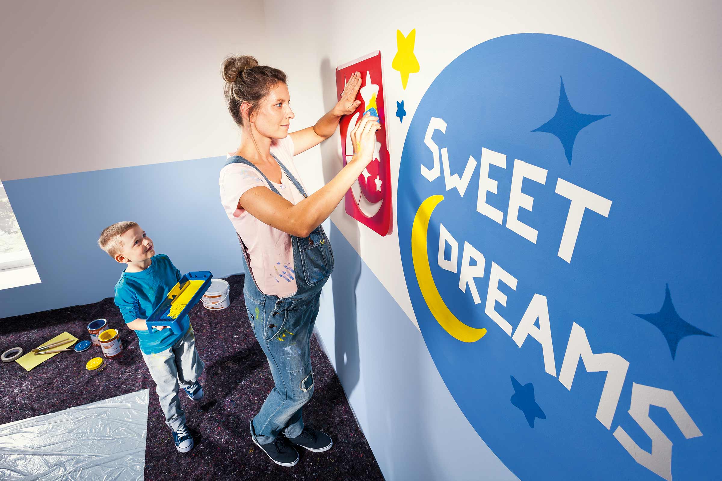 Een vrouw en een kind decoreren een kinderkamerwand met een sjabloon en verf.