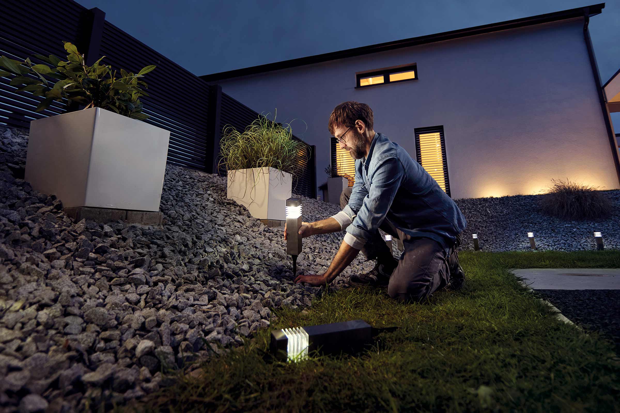 Een man installeert tuinverlichting in een tuin met grind en planten