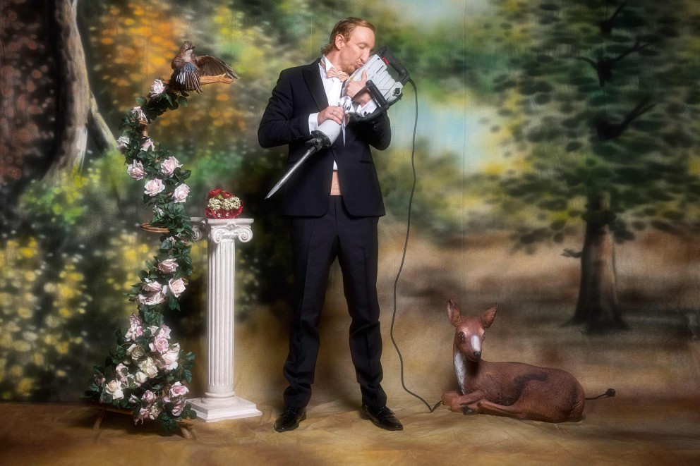 Man in pak omhelst breekhamer voor geschilderde achtergrond met bloemen en dierenfiguren