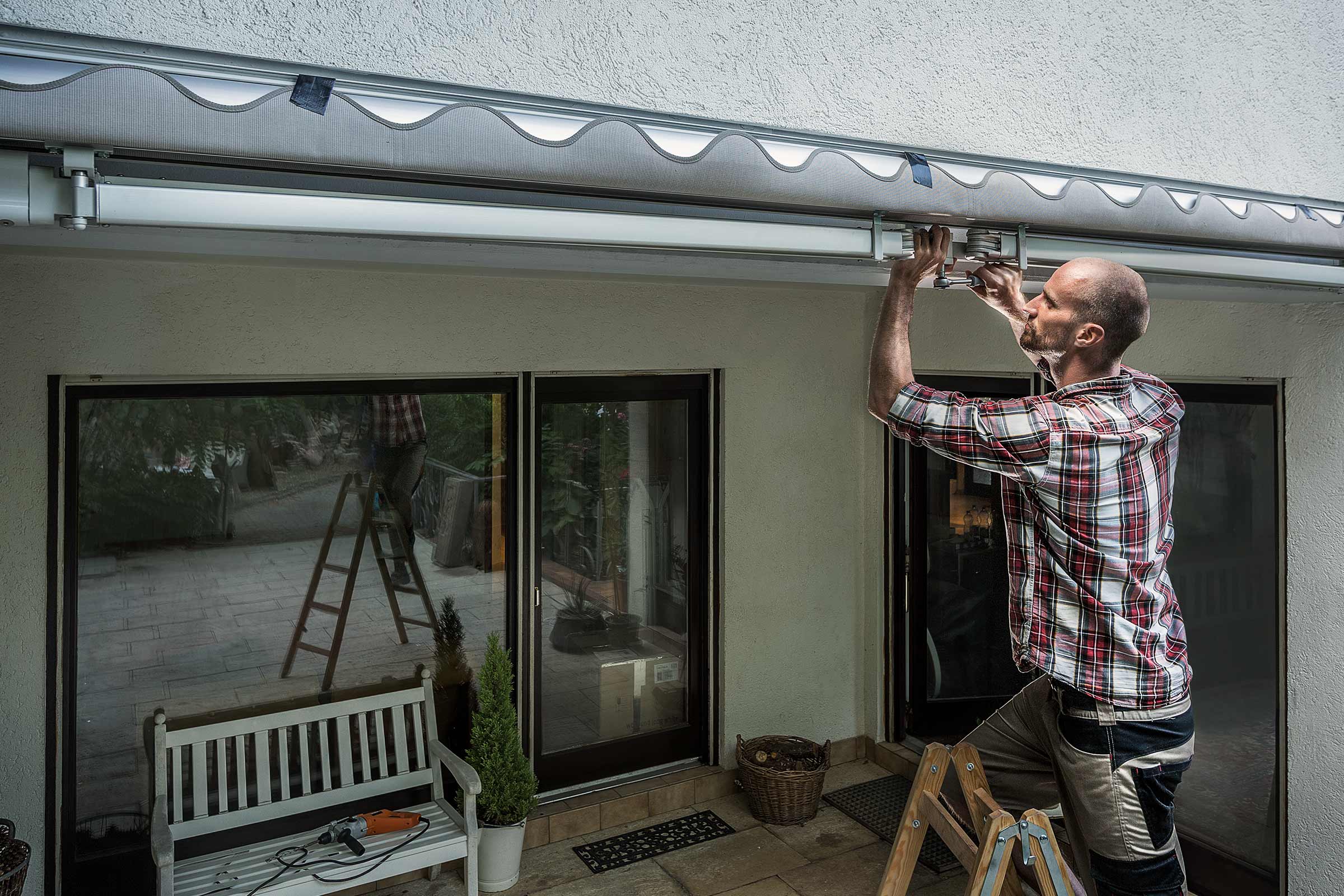 Een man monteert een zonnescherm aan een huismuur boven een terrasdeur.