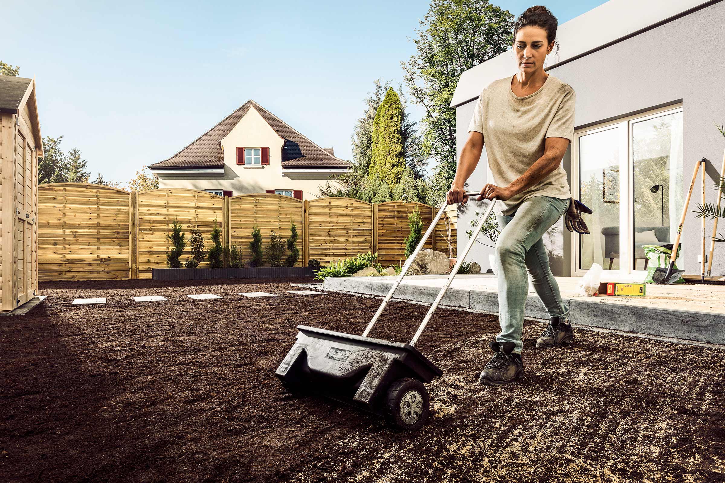 Een vrouw gebruikt een zaadstrooier om gazonzaden in de tuin te verspreiden.