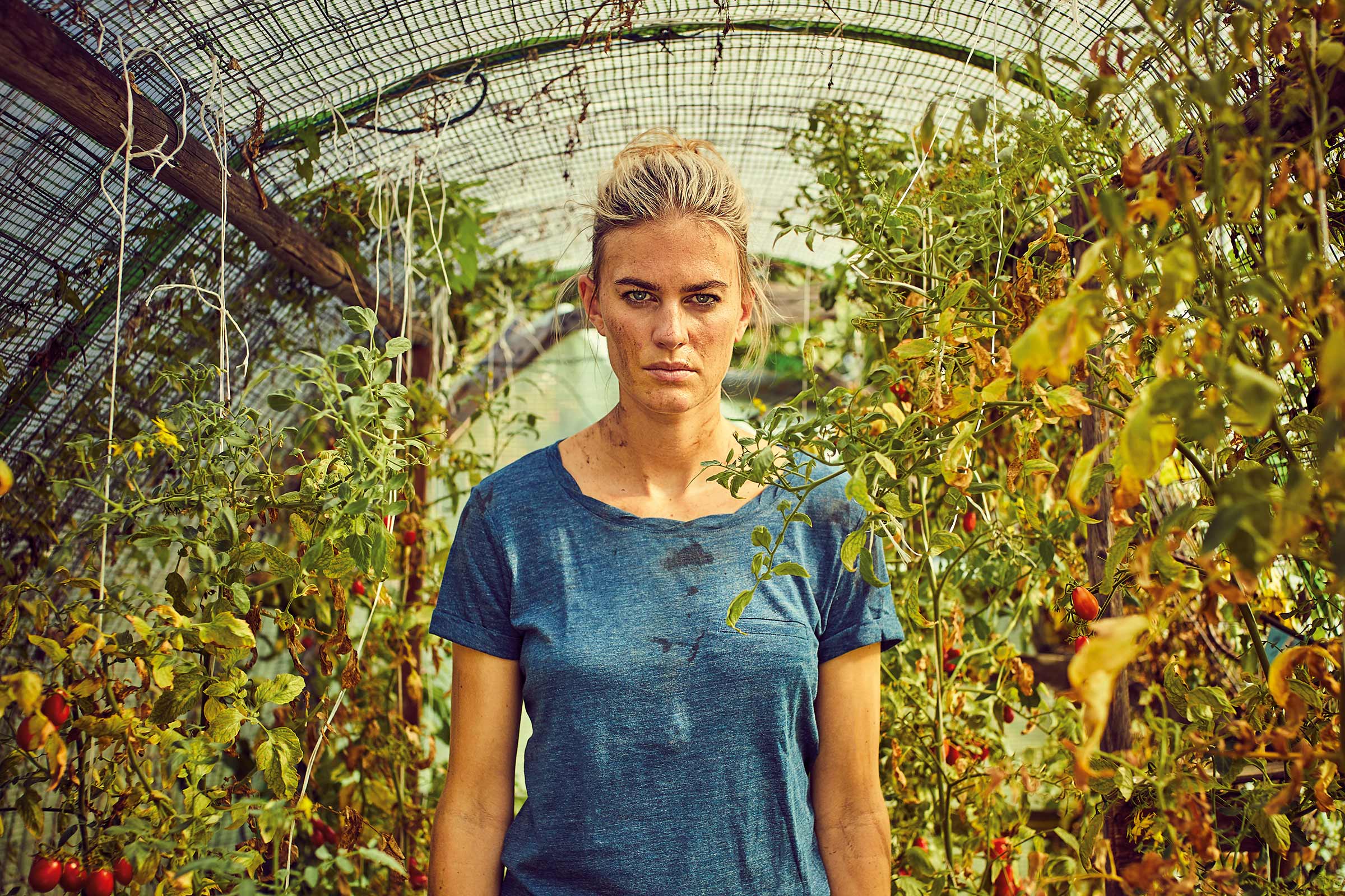 Een vrouw staat in een kas tussen tomatenplanten.