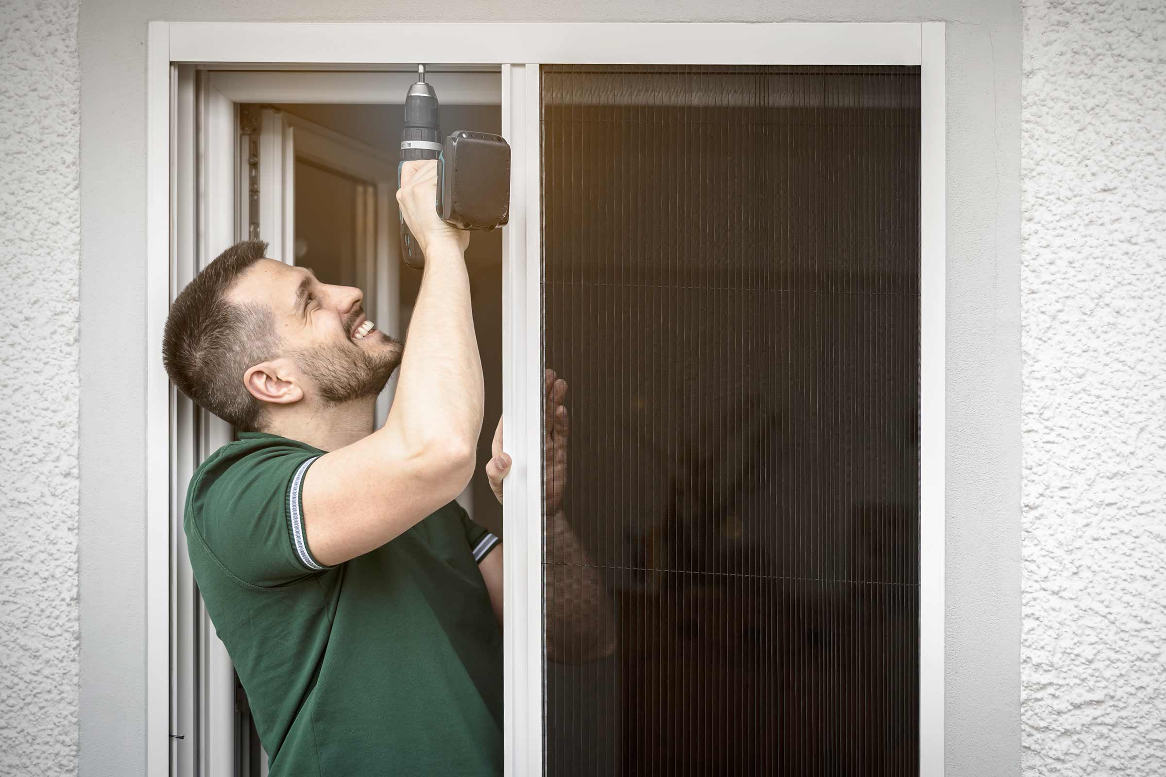 Man installeert een insectenhor met een accuschroevendraaier op een raam