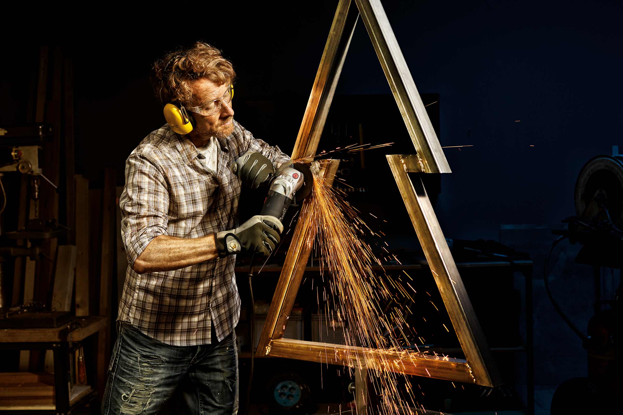 Man slijpt metalen constructie met haakse slijper, vonken vliegen eraf, persoonlijke beschermingsmiddelen worden gedragen.