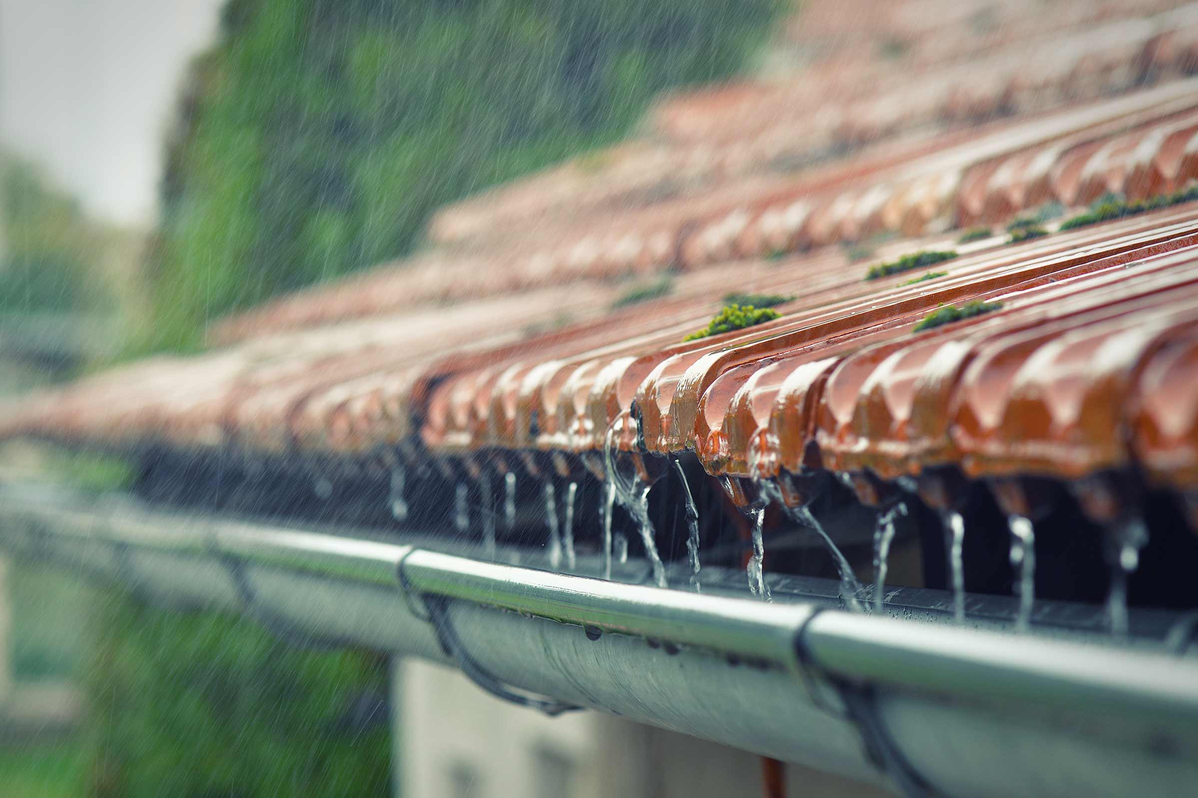 Regenwater stroomt van een dak met dakpannen in een dakgoot