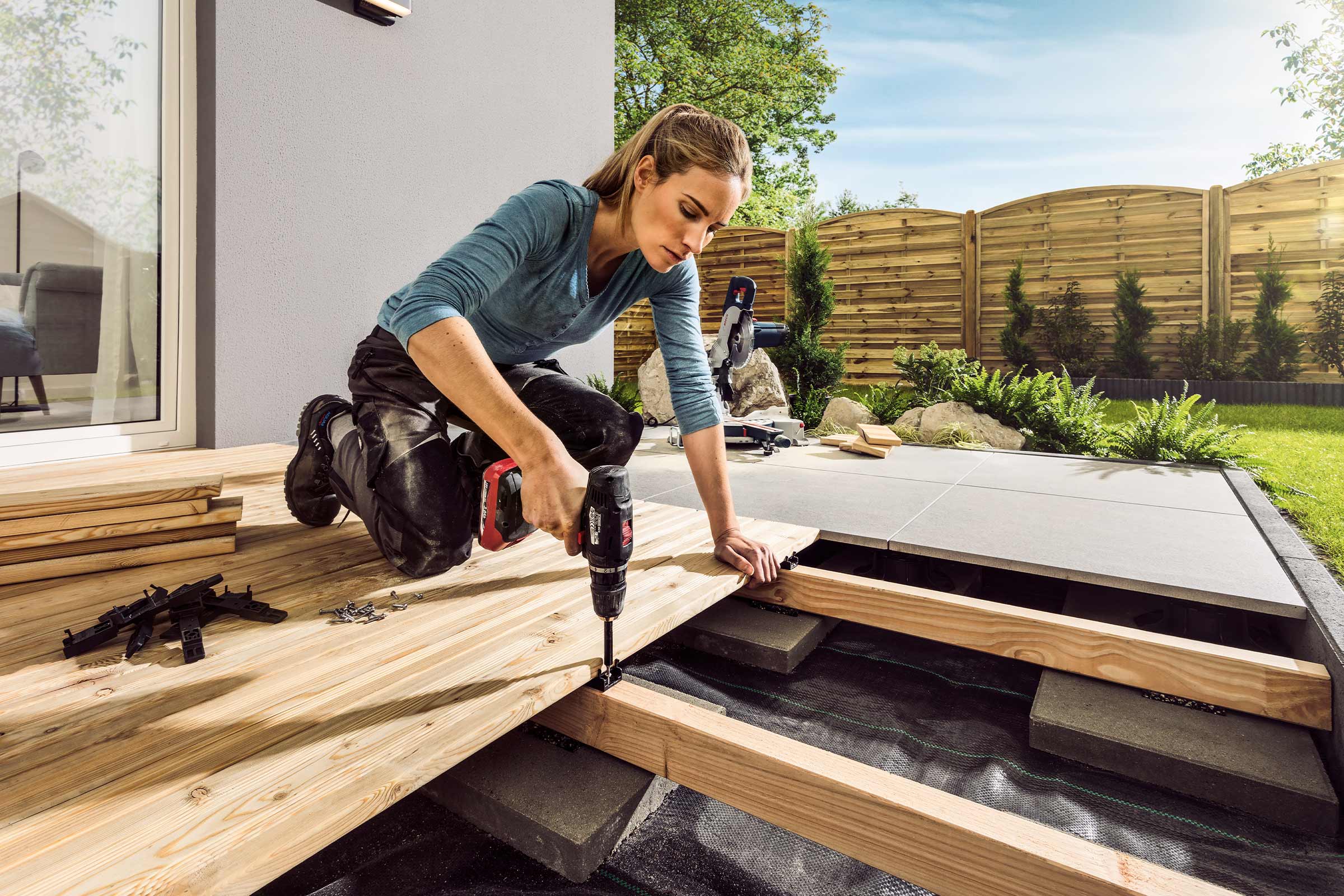 Vrouw monteert een houten terras met een accuschroevendraaier in de tuin.