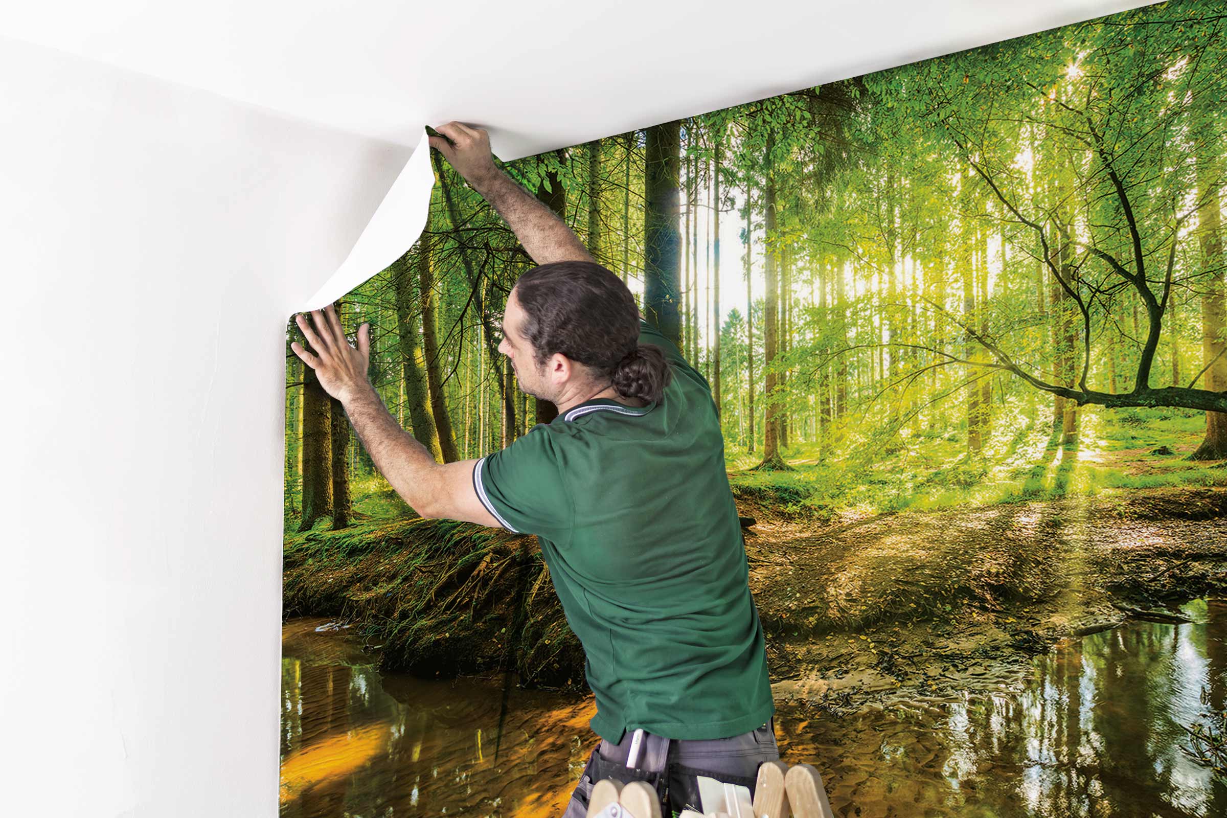 Een persoon bevestigt een fotobehang met een bosmotief aan een muur.
