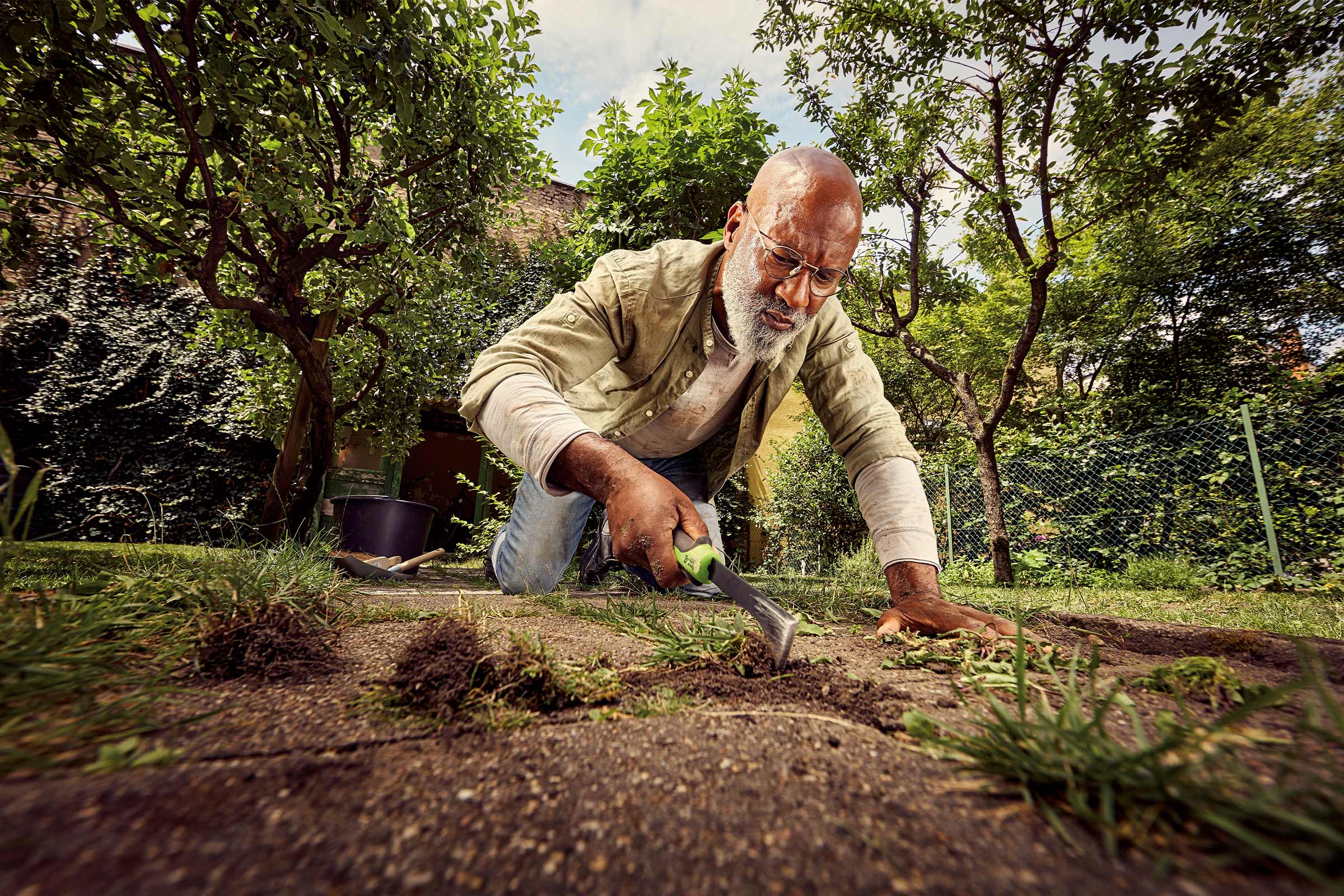 Een man knielt in de tuin en gebruikt een handgereedschap voor gazononderhoud.