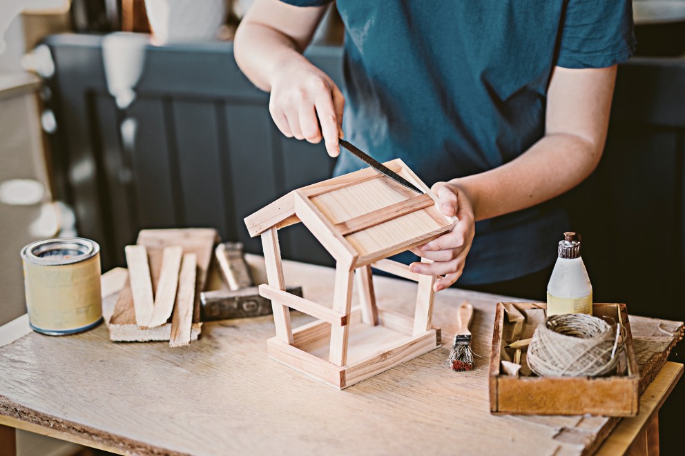 Iemand vijlt aan een houten vogelhuisje op een tafel met gereedschap.