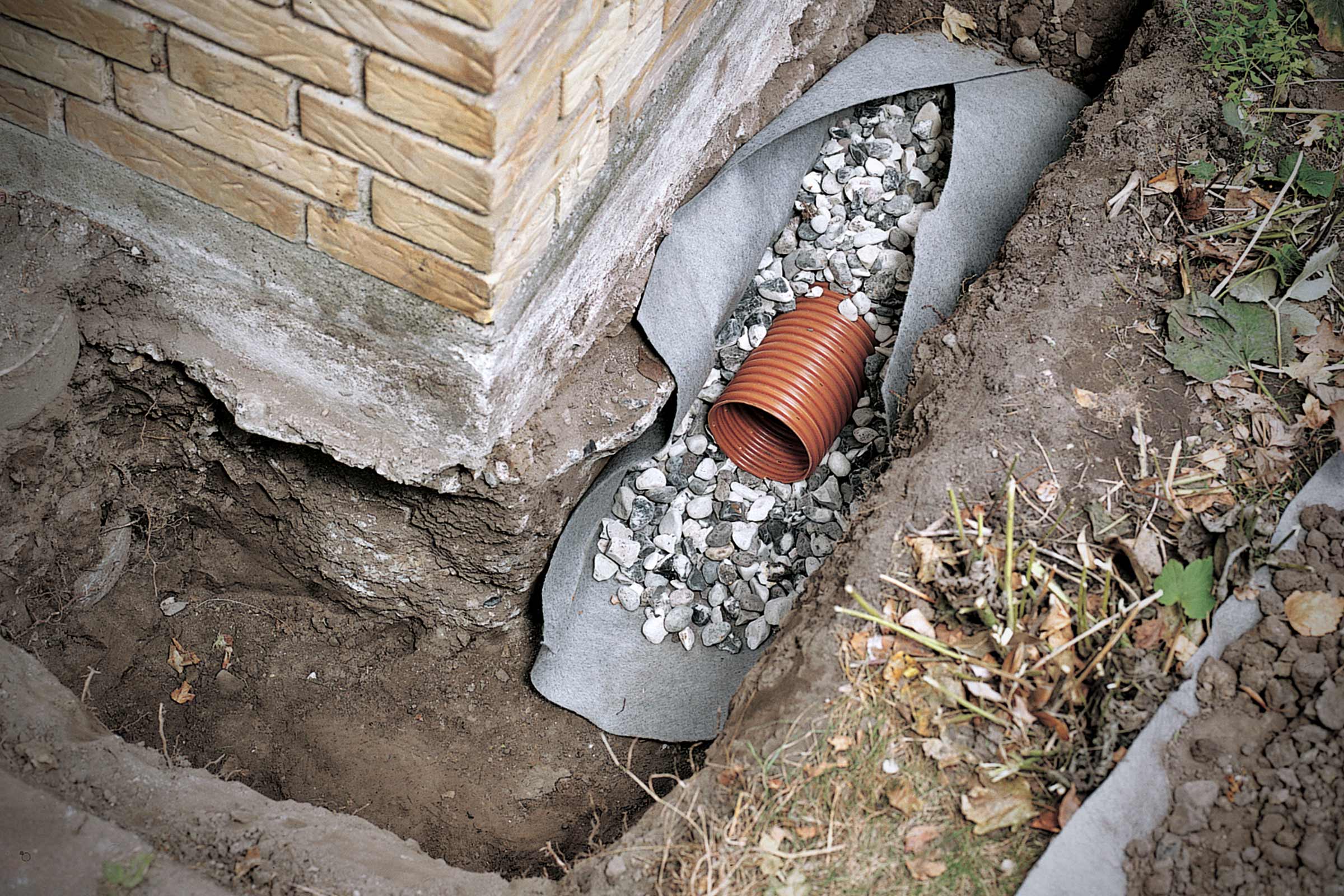 Drainagegreppel met drainagebuis en grind ter bescherming van een gebouw.