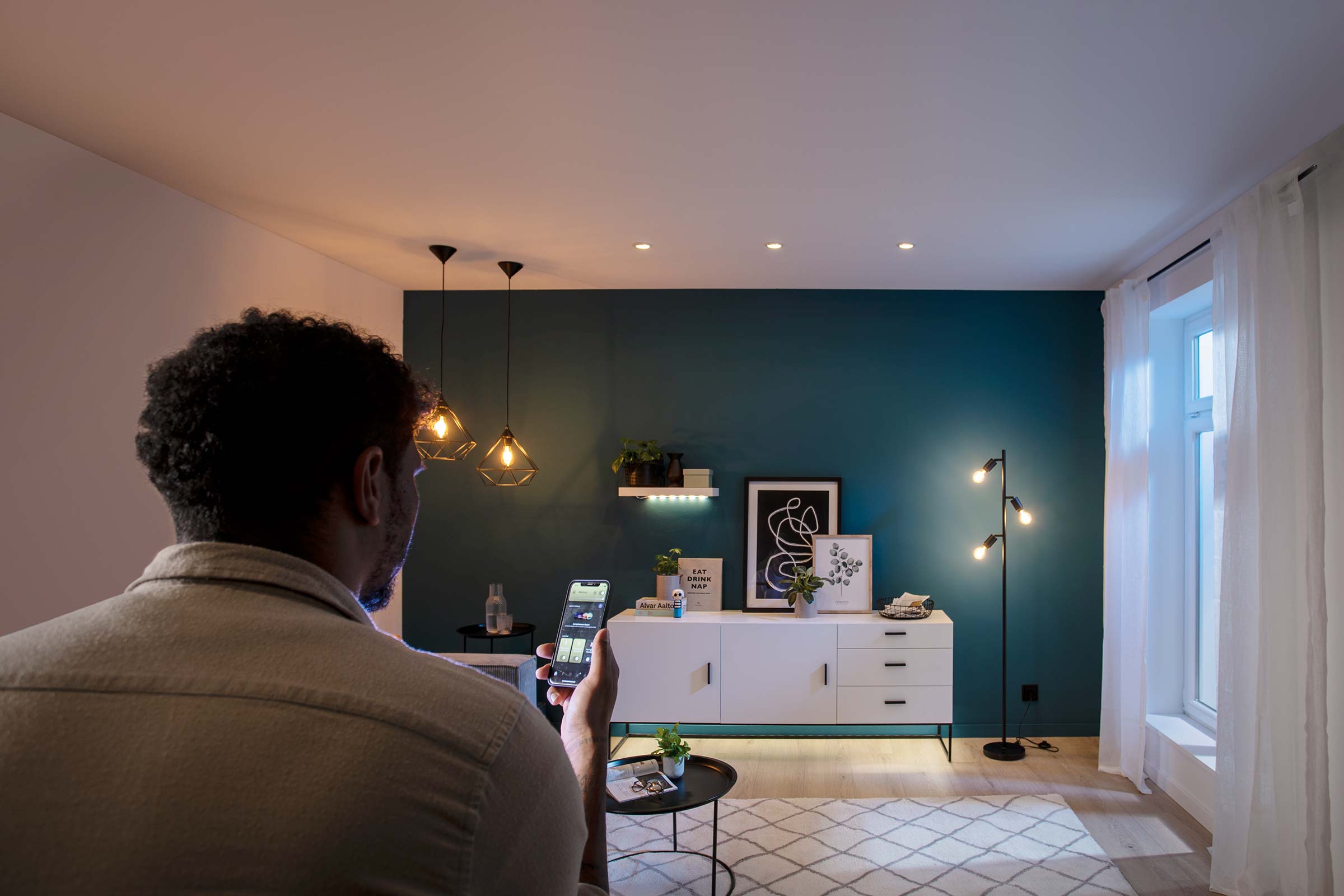 Man bedient verlichting in de woonkamer met een app op zijn smartphone