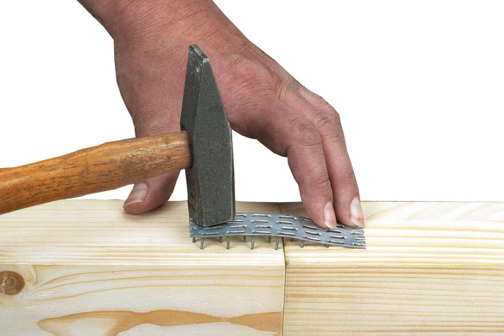 Een vakman bevestigt een nagelplaat met een hamer aan twee stukken hout.