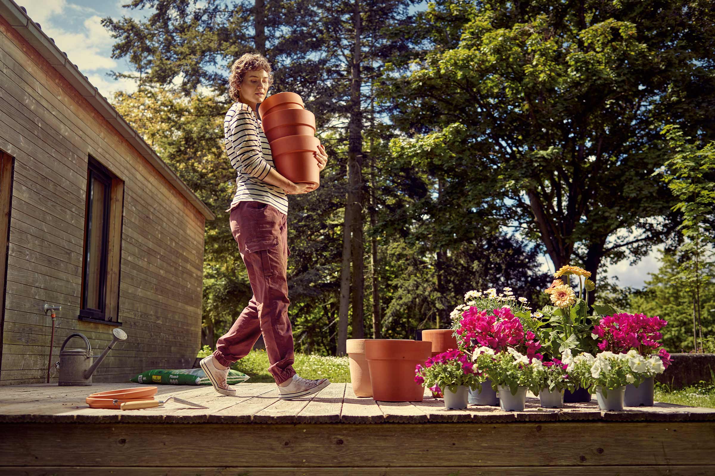 Vrouw draagt plantenbakken in de tuin op een houten terras
