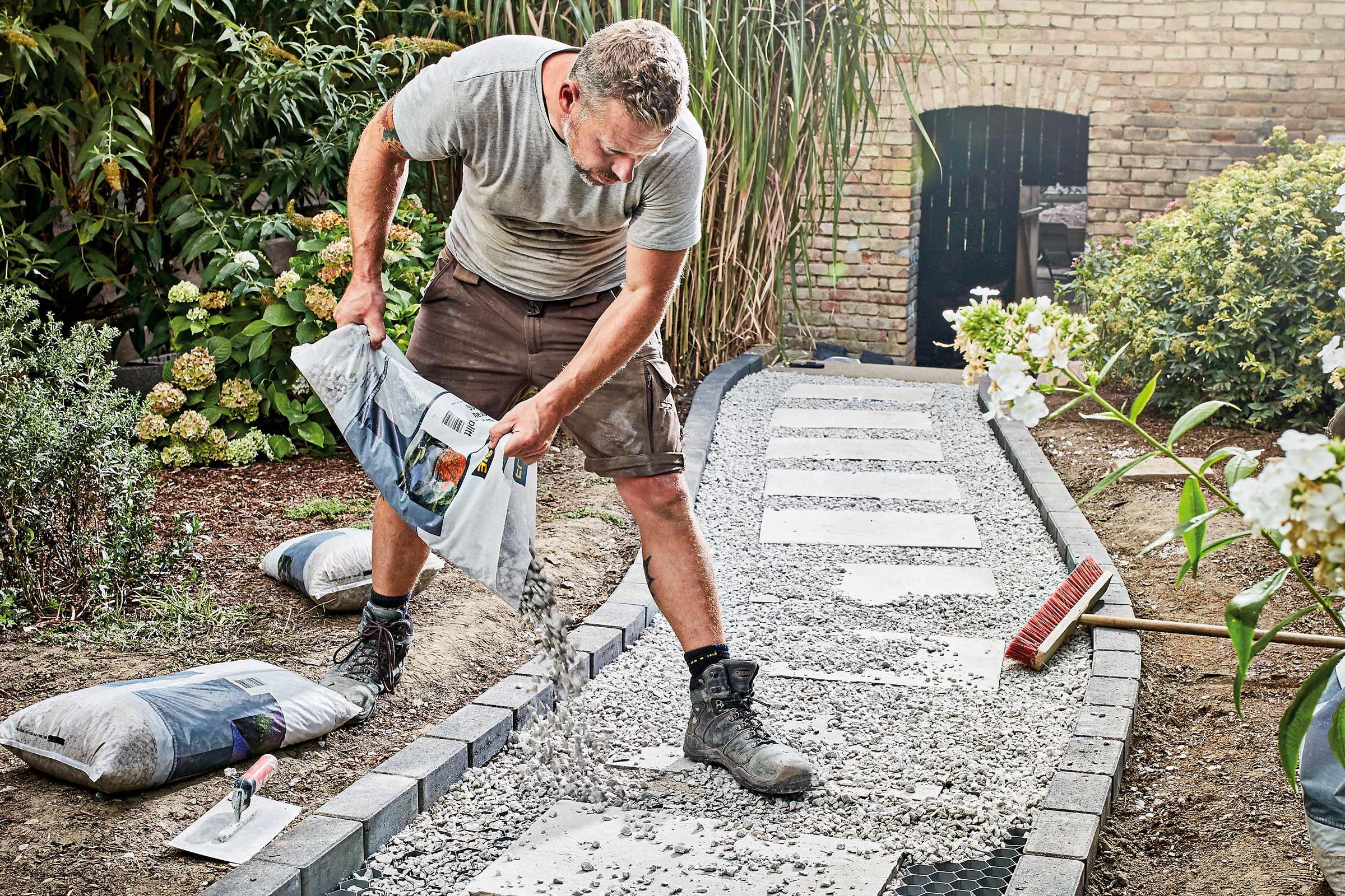 Man stort grindpad in de tuin met decoratief grind uit een zak