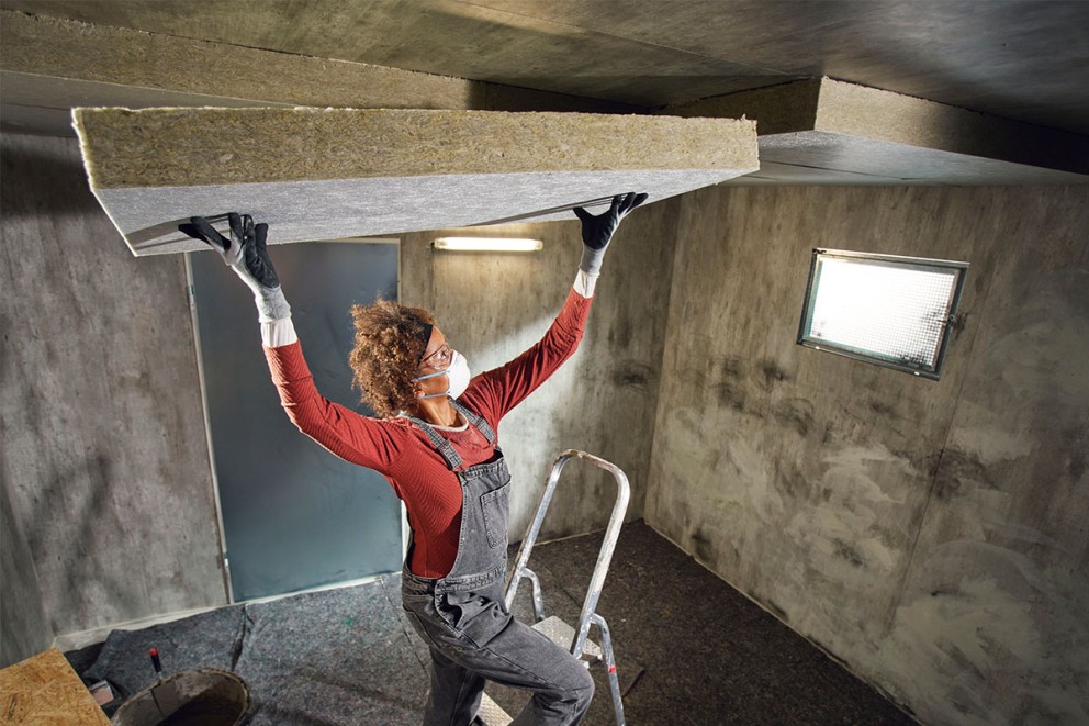 Vrouw monteert isolatieplaat aan kelderplafond met ladder en beschermende kleding