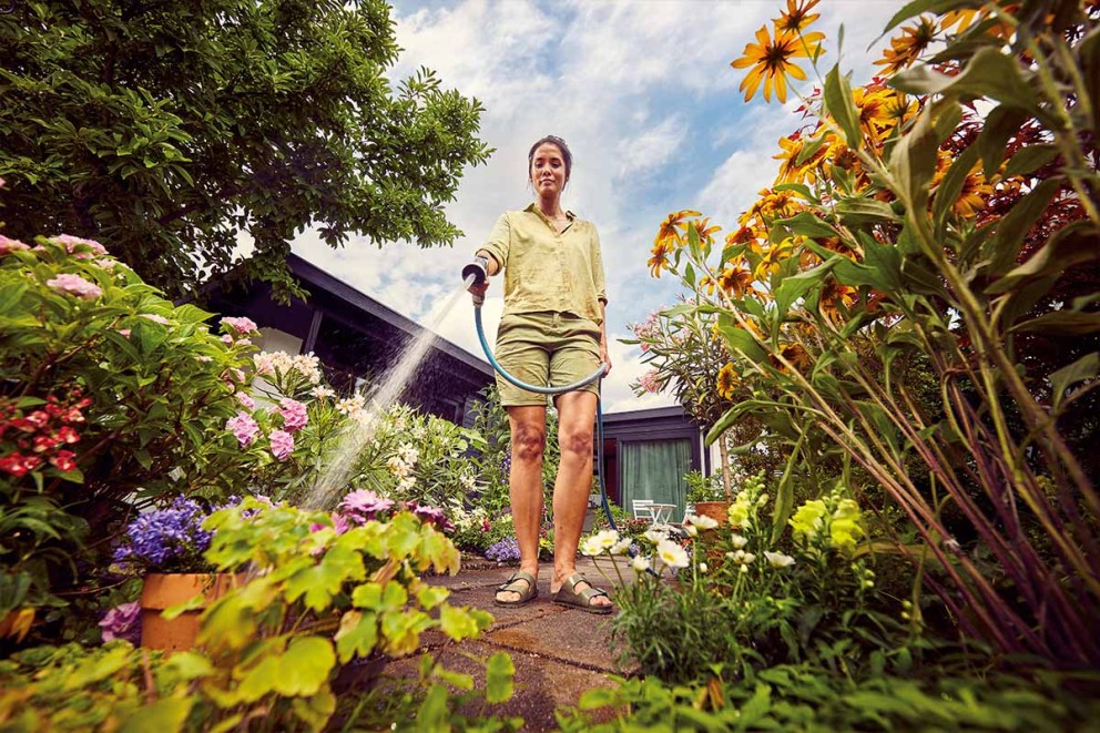 Vrouw besproeit bloemen in de tuin met een tuinslang.