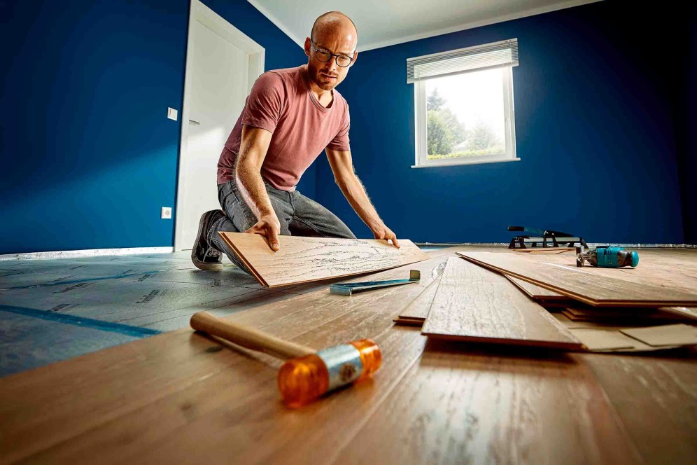 Man legt laminaatvloer in kamer met gereedschap zoals hamer, trekijzer en decoupeerzaag.