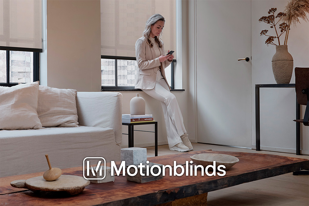 Lichte woonkamer met rolgordijnen, bank en een vrouw die een mobiele telefoon gebruikt