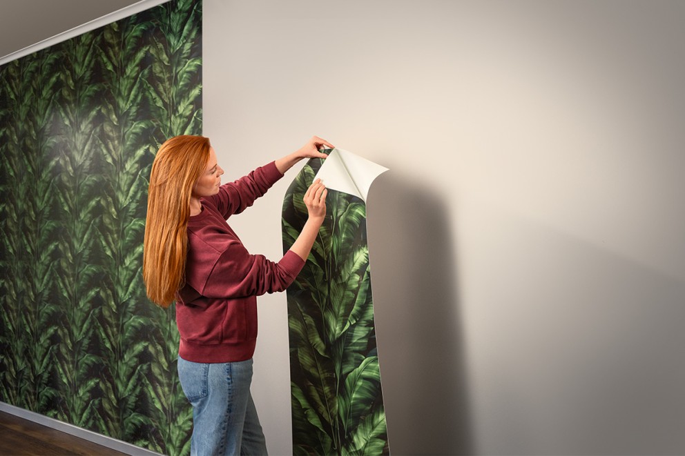 Vrouw brengt een vliesbehang met plantenpatroon aan op de muur