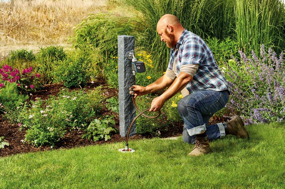 Man sluit een tuinslang aan op een kraan in de tuin