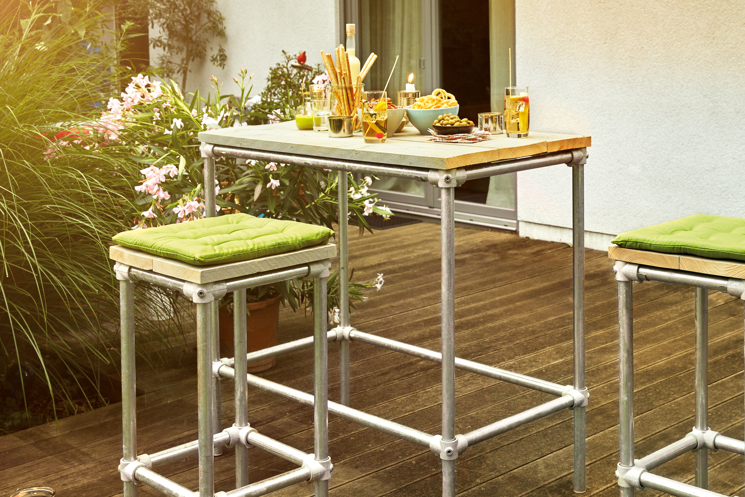 Tuinscène met een bartafel en barkrukken van metalen buizen en hout met snacks en dranken