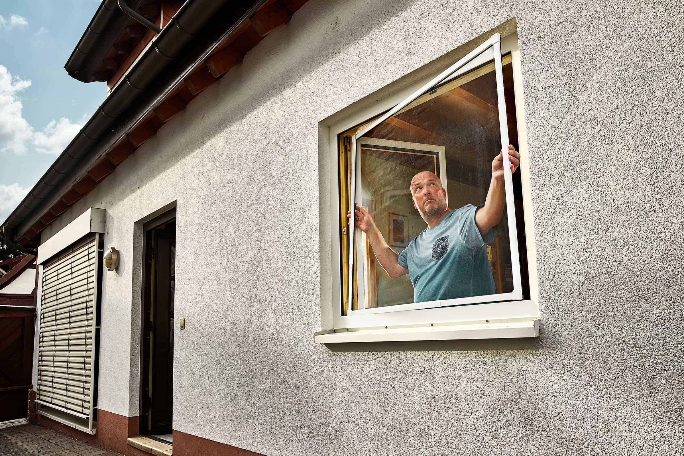 Man installeert een insectenhor in een raam van een huis.