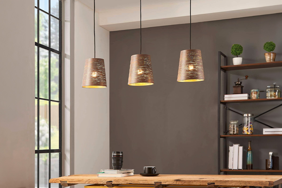 Drie metalen hanglampen hangen boven een houten tafel in een kamer.