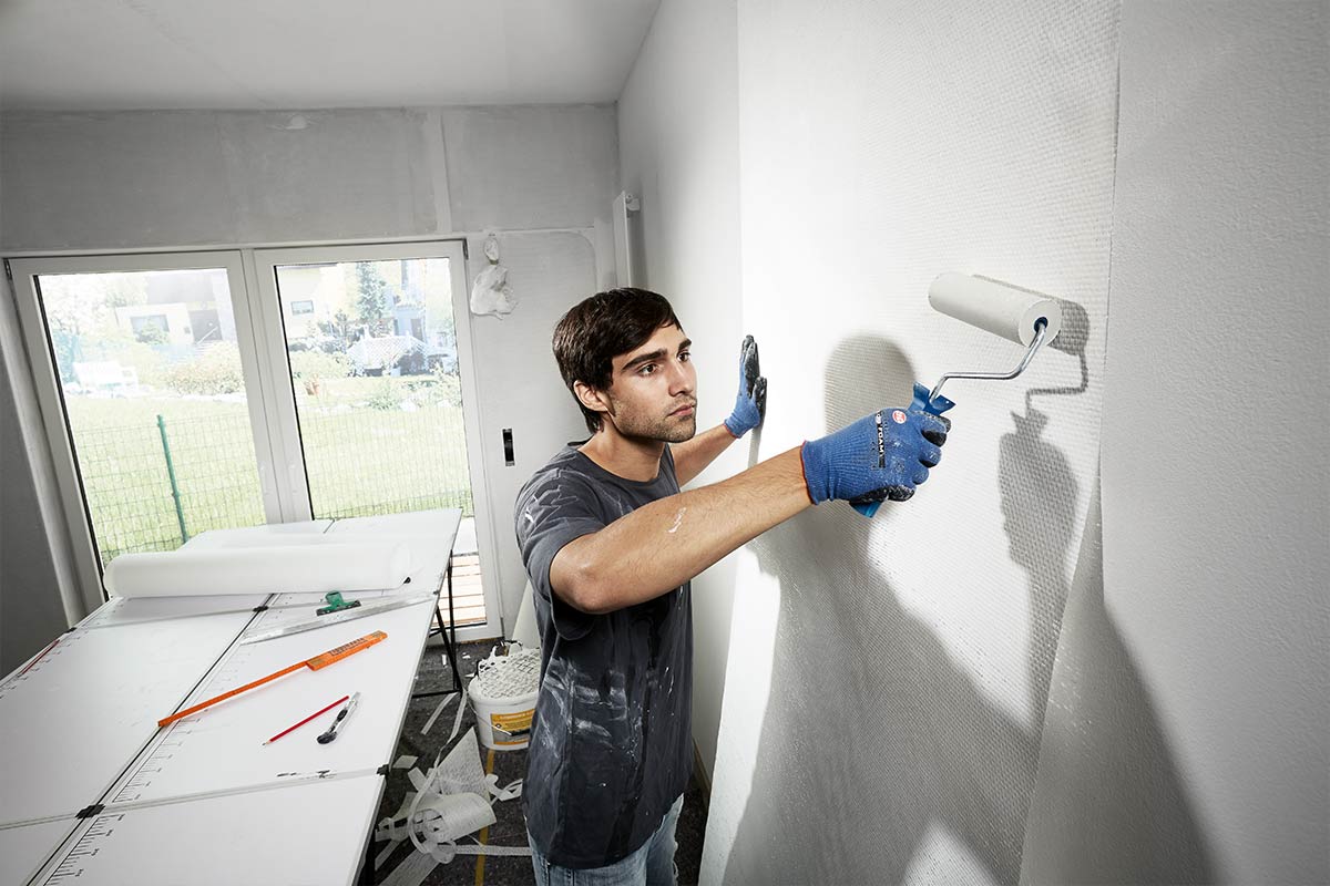 Man schildert een muur met een verfroller in een heldere kamer.