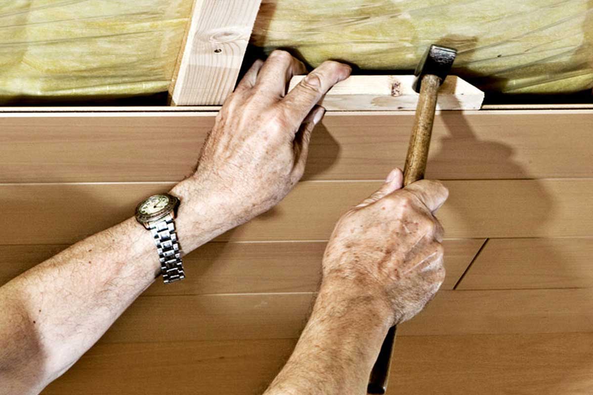 Een persoon bevestigt houten latten aan het plafond van een kamer met een hamer.