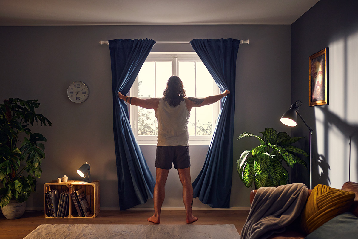 Man opent blauwe gordijnen bij het raam in een ingerichte kamer