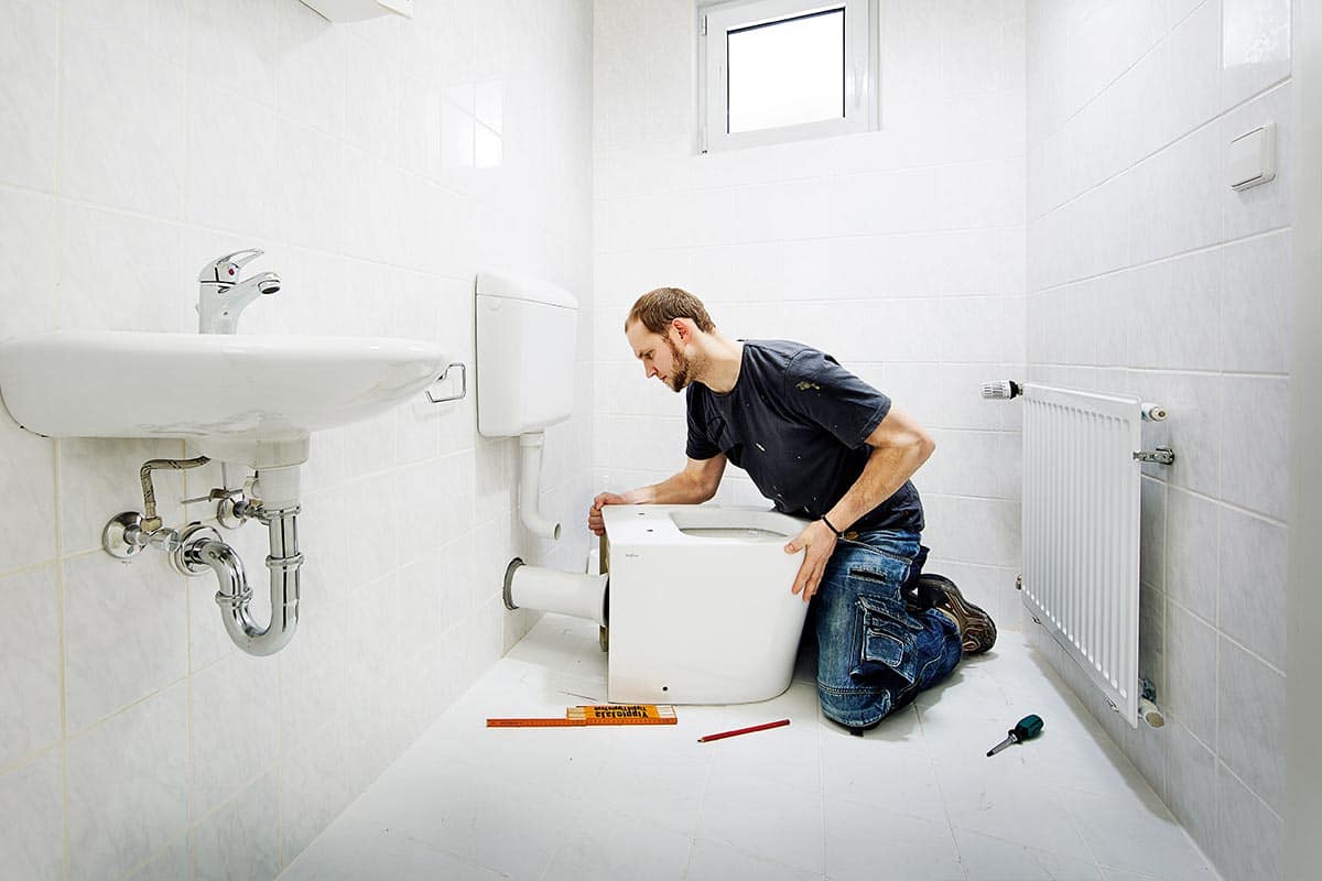 Installateur installeert toilet in een lichte badkamer met wastafel en radiator.