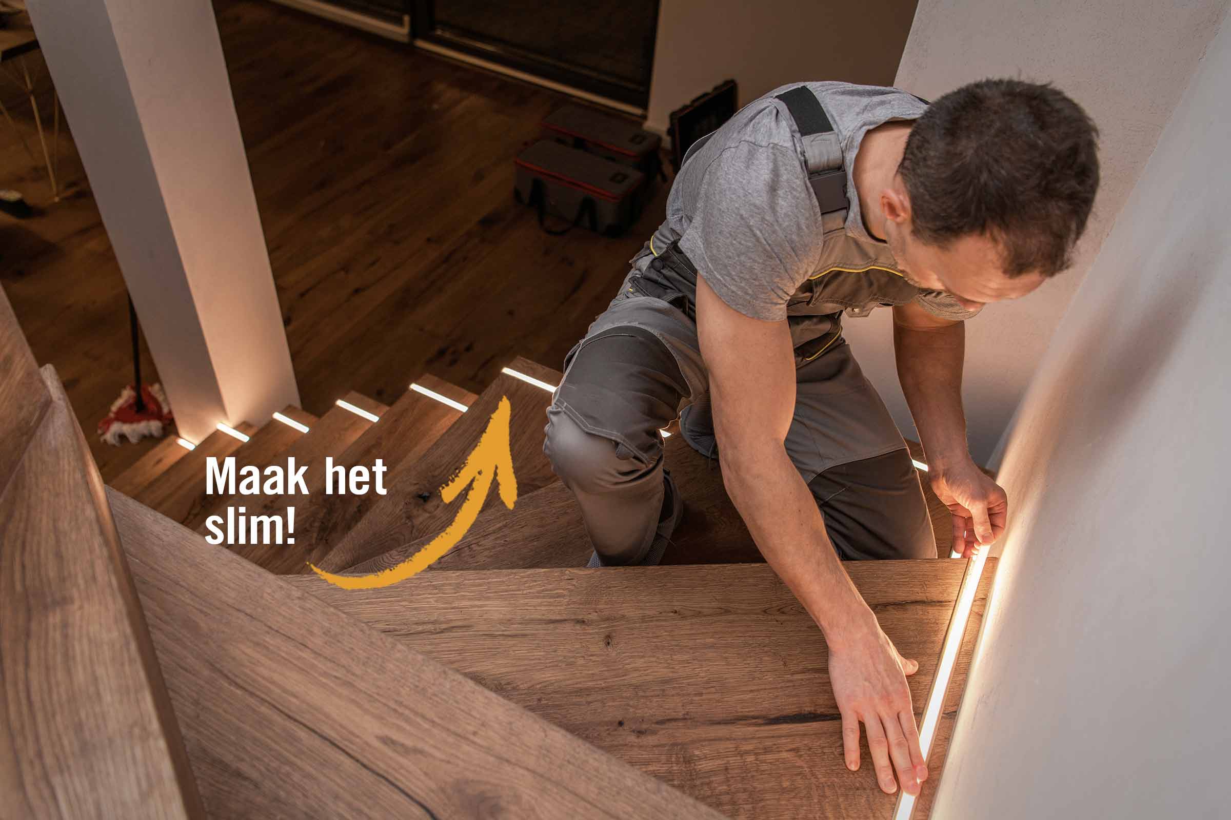 Een man installeert ledverlichting op een houten trap om de trap te accentueren.