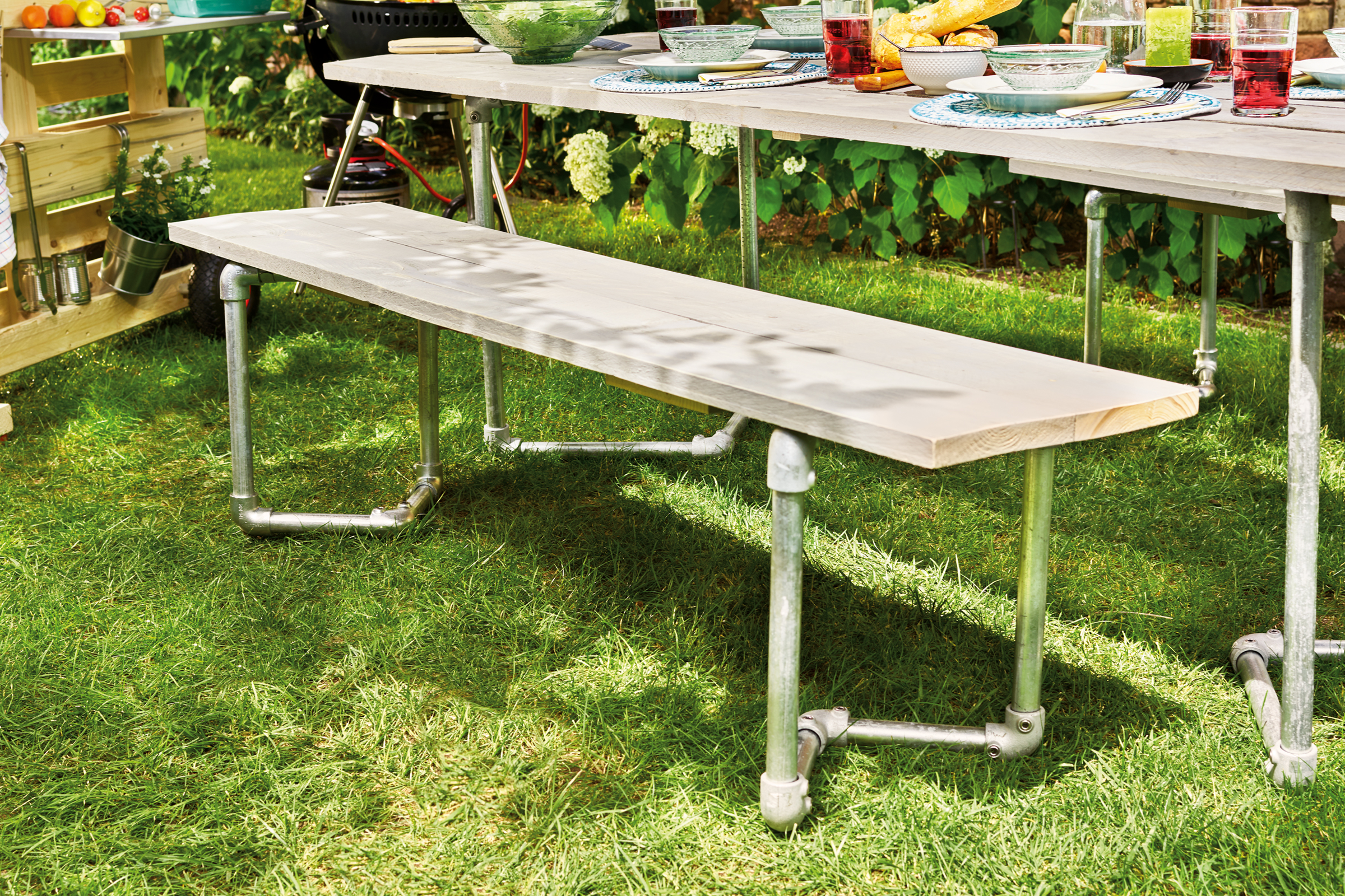 Tuinscène met houten tafel en bank met metalen poten op gazon