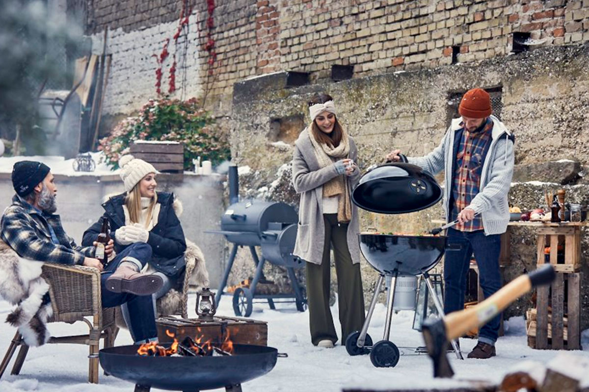 Barbecuescène in de winter met houtskoolbarbecue, vuurkorf en meerdere personen buiten voor een bakstenen muur