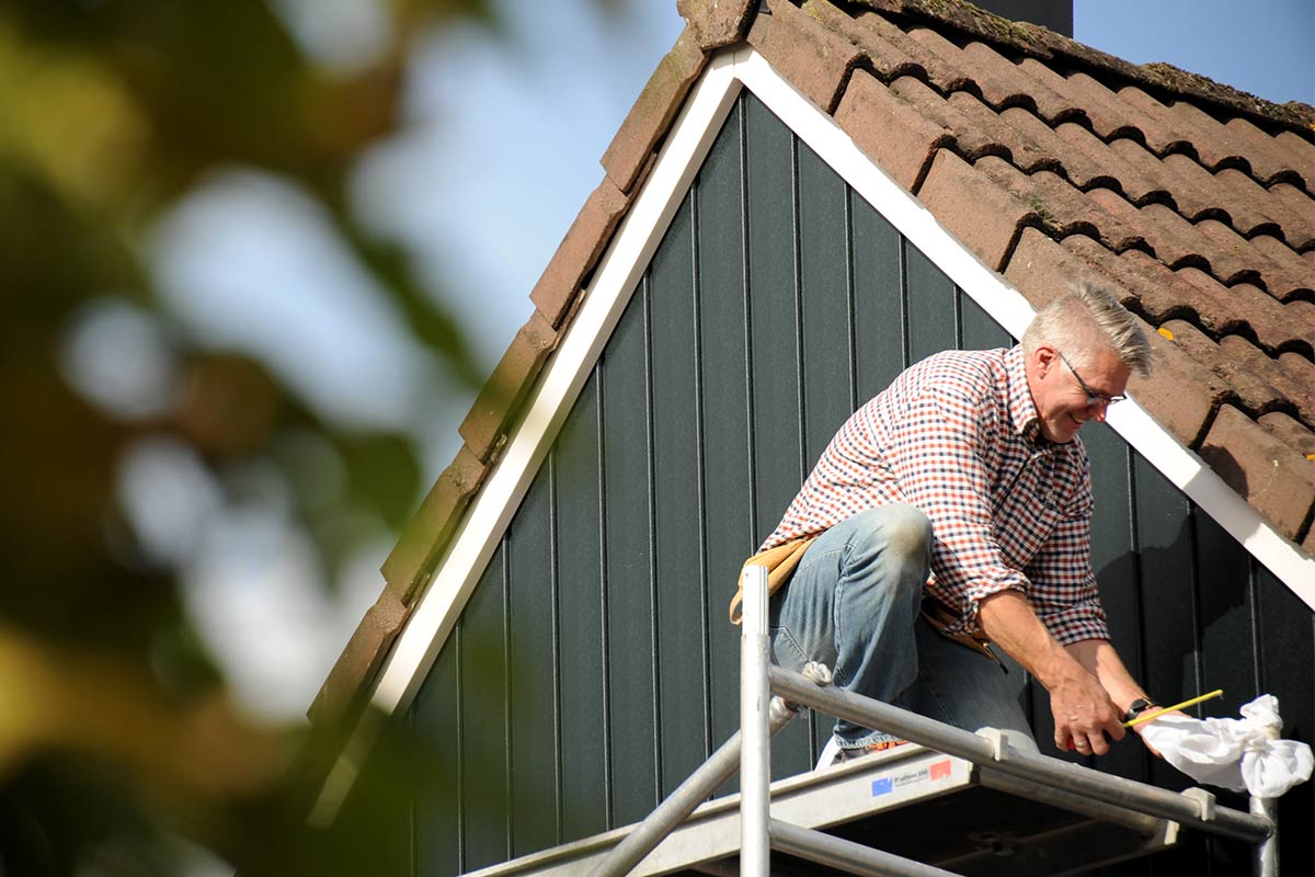 Een man reinigt de gevel van een huis vanaf een steiger.