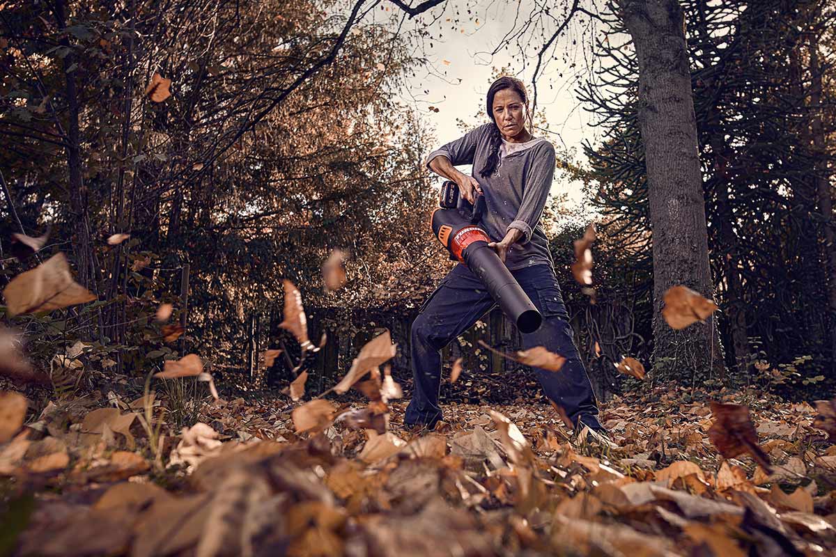 Vrouw gebruikt een bladblazer in de tuin om herfstbladeren te verwijderen.